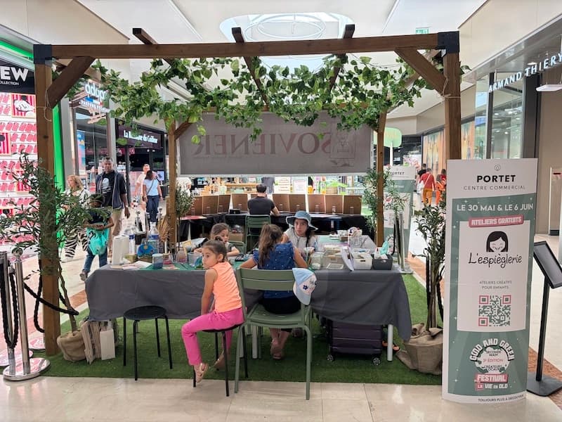 Le stand de L'Espièglerie au Good & Green Festival du centre commercial Portet, des enfants en atelier sous une pergola végétale