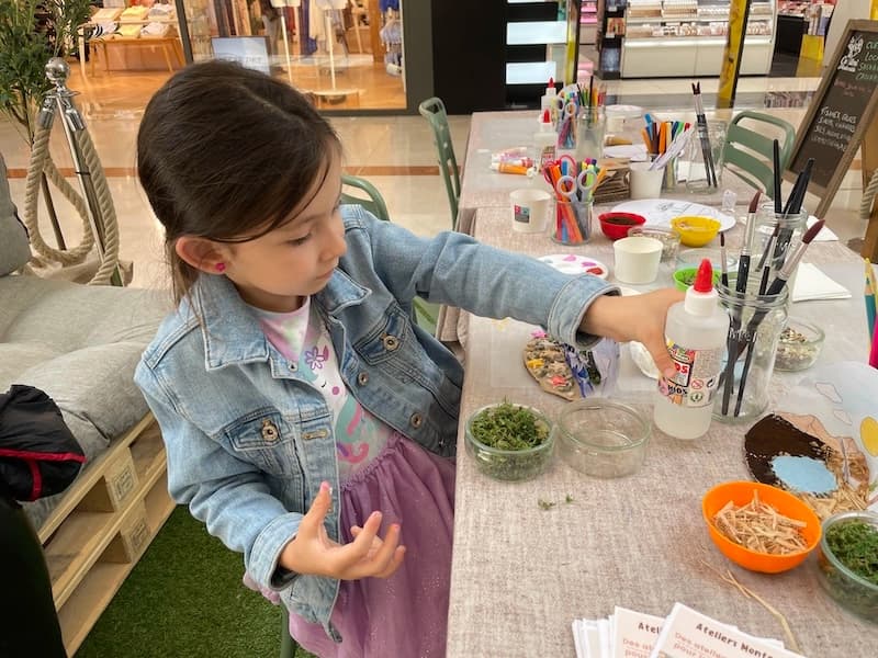 Une petite fille colle de la mousse et des éléments naturels sur sa création