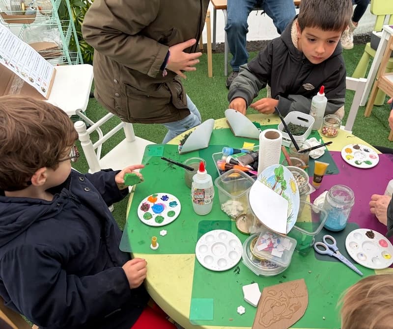 Des enfants peignent et collent leurs créations autour d'une table d'atelier aux Serres municipales