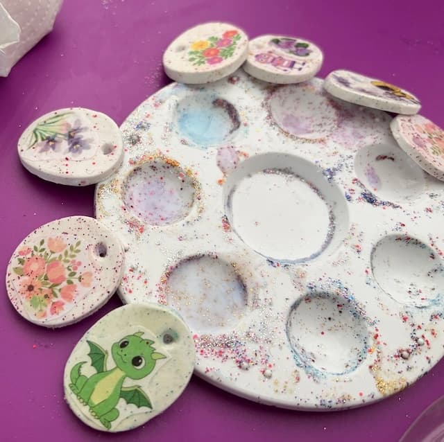 Médaillons en argile décorés de fleurs et d'un petit dragon, posés autour d'une palette pailletée