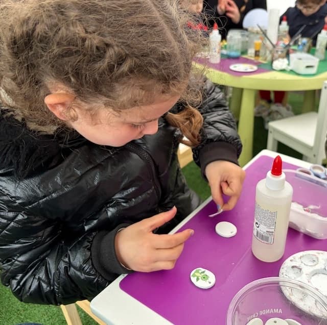 Une petite fille décore un médaillon en argile à la table d'atelier