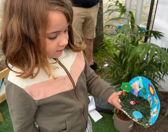 Une petite fille montre son jardin miniature en mousse sur un disque peint