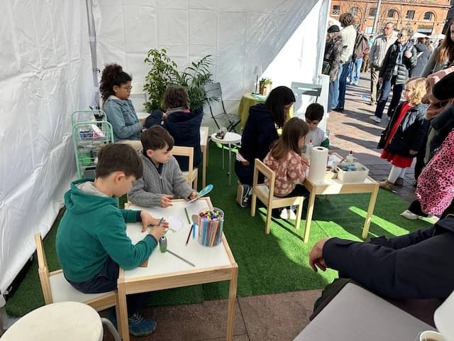 Des enfants dessinent à de petites tables sous la tente d'atelier de L'Espièglerie, place du Capitole