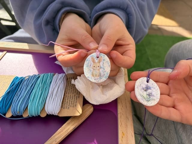 Deux enfants montrent leurs pendentifs en argile décorés d'un lapin et d'une violette