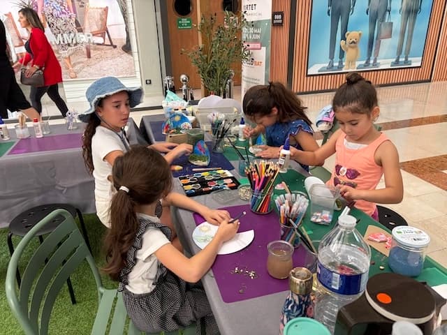 Quatre enfants peignent et décorent leurs créations autour d'une table d'atelier au Good & Green Festival