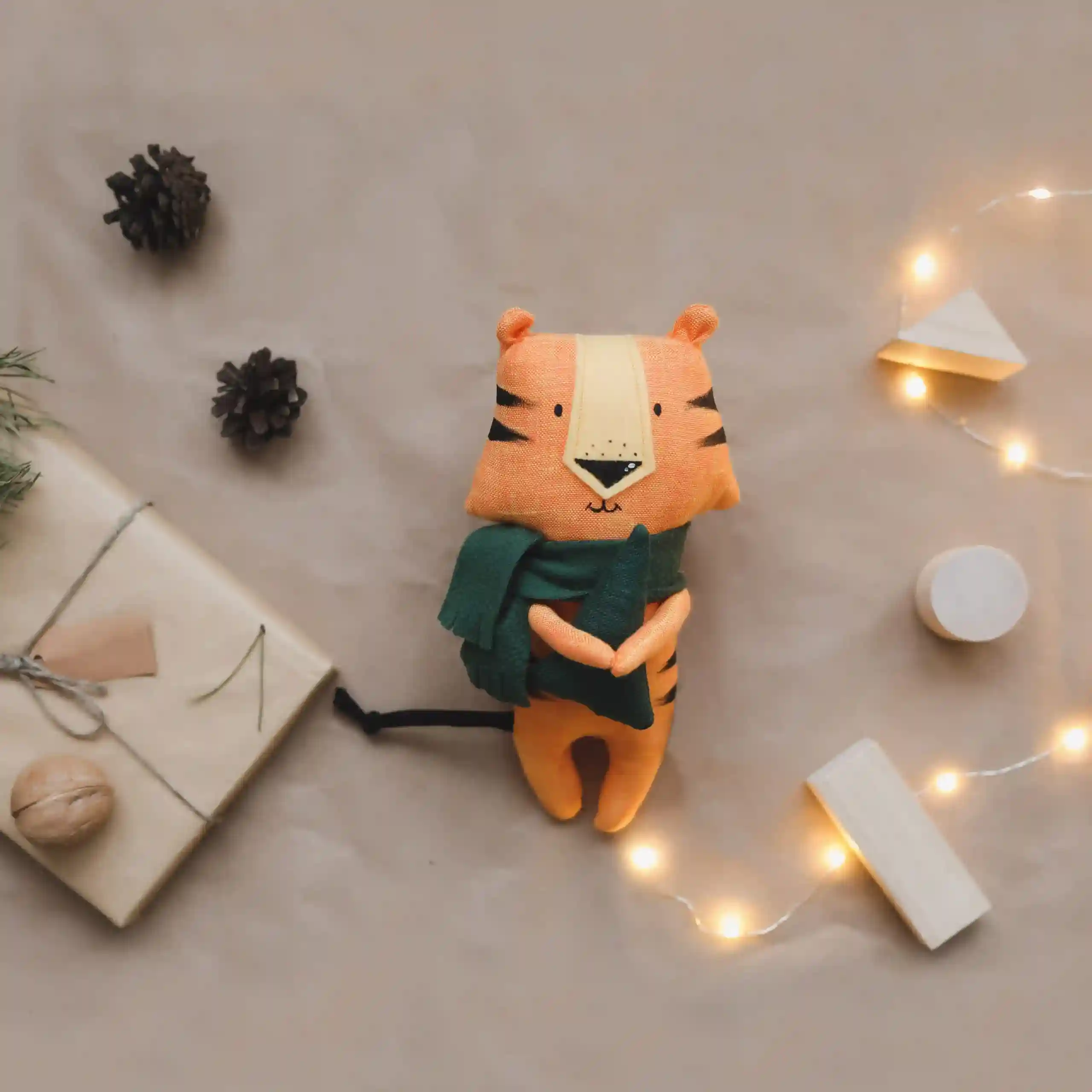 Un tigre en tissu au pied du sapin de Noel avec un paquet cadeau nous regarde